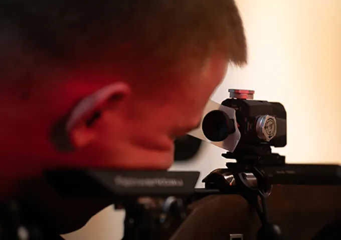 A person looking through a scope or sight mounted on a competition air rifle or small-bore rifle.