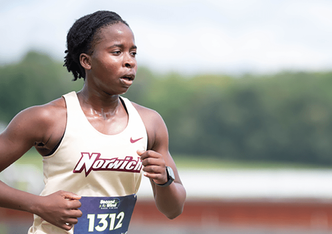 A close-up of a young woman runner in a white and gold jersey with the word "Norwich".