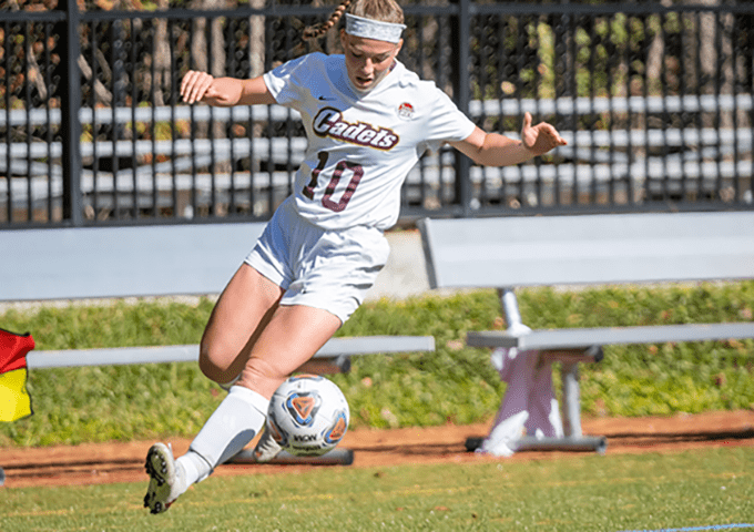 Female soccer player wearing number 10 Cadets jersey strikes the ball during daytime match, showcasing athletic form on a sunny field.