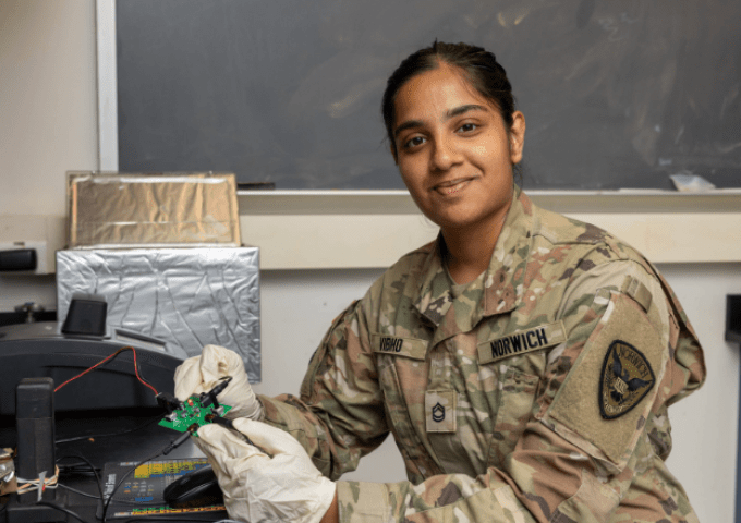 Student in science lab and wearing military uniform while she works on a technical project.