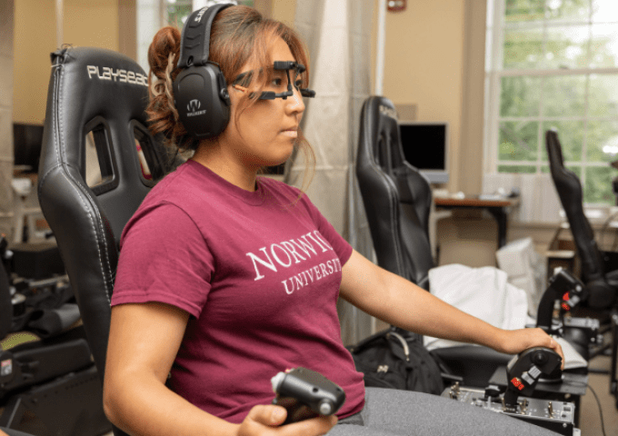 Student sitting in chair with a headset on and flight simulator gear on looking at screen.