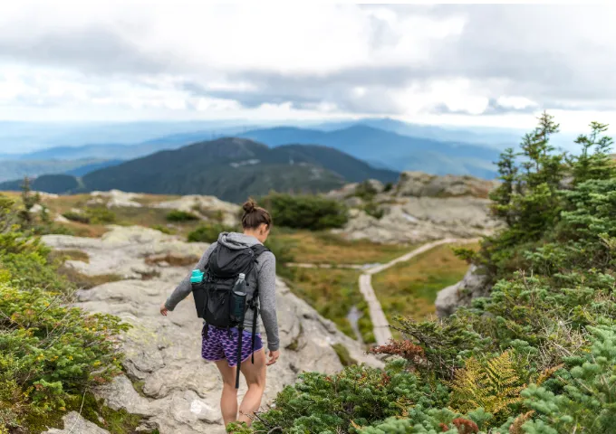 Hiker walking on the ridgeline trail surrounded by a view of the Green Mountains.