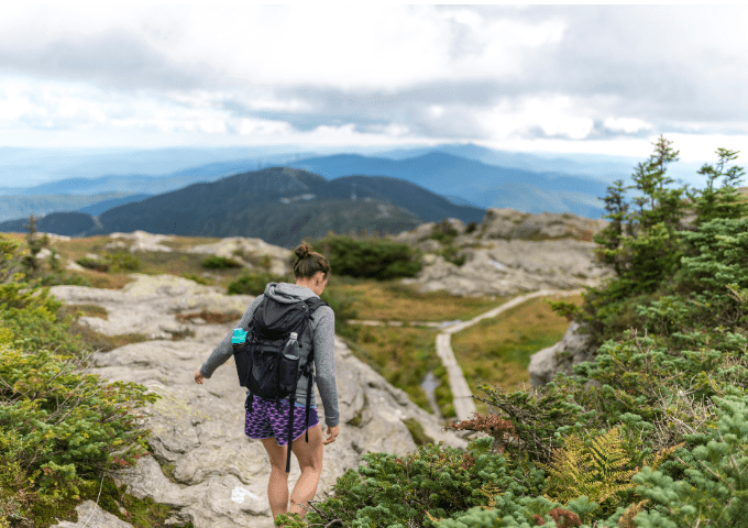 Hiker walking on the ridgeline trail surrounded by a view of the Green Mountains.