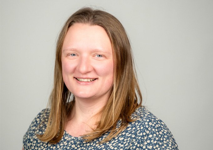Person with medium colored straight shoulder length hair, light complexion, wearing a green patterned shirt.