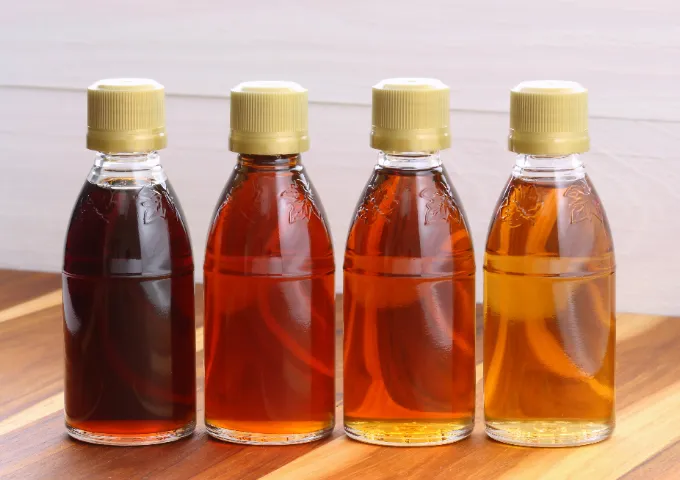 A line of clear maple syrup jars showing the different amber grades.