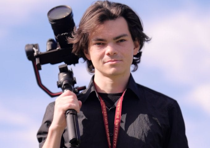 Student holds camera stabilizer outdoors while wearing a Norwich University lanyard.