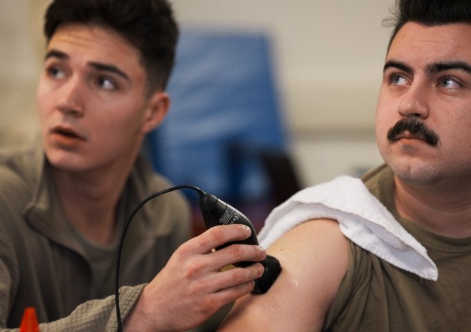 Student uses a handheld ultrasound device on another student's upper arm during a classroom training session.