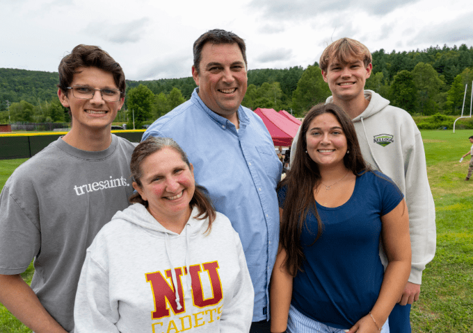 Norwich family posing together in front of the baseball field with green mountains in the background.