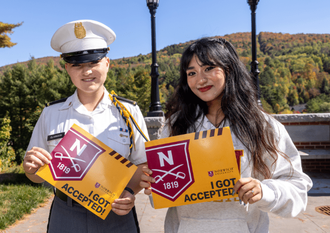 A Corps student and civilian student stand together showing off their accepted letters and smiling.