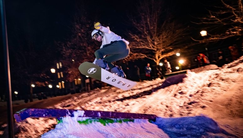 Norwich student snowboarder mid-air flying over a rail.