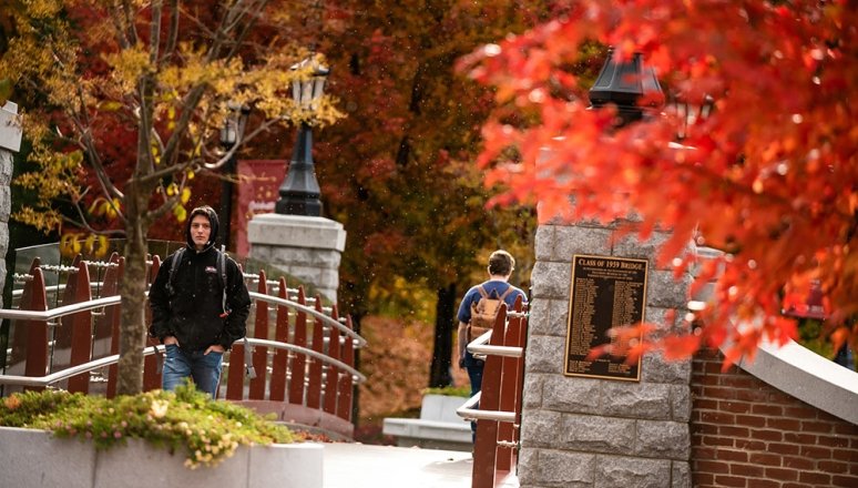 Fall foliage surrounding civilian students as they walk across the Alumni Bridge