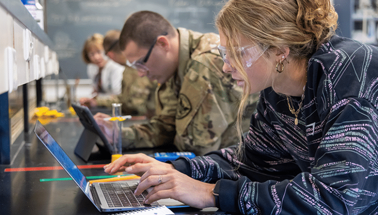 Civilian student working in a science lab on her laptop.