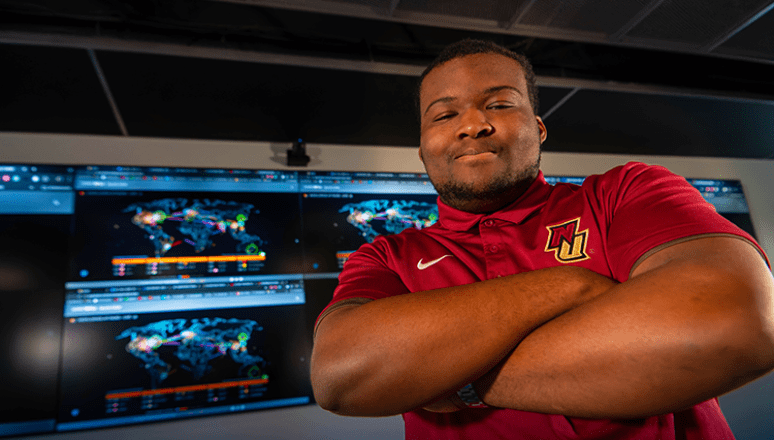Student standing in front of large cyber screens inside the war room.