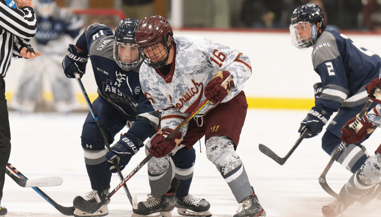 Hockey players in digital camo, and navy jerseys battling for puck, intense struggle at face-off circle.