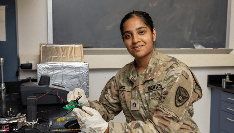 Student in science lab and wearing military uniform while she works on a technical project.