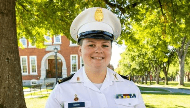 Elizabeth Scalf '23 standing on campus in uniform, smiling.