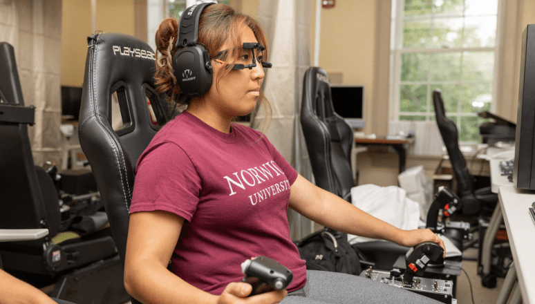 Student sitting in chair with a headset on and flight simulator gear on looking at screen.