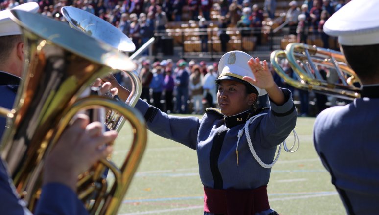 Drum major leads brass players at a stadium.