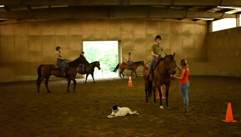 Group of cadets practice riding in indoor arena.