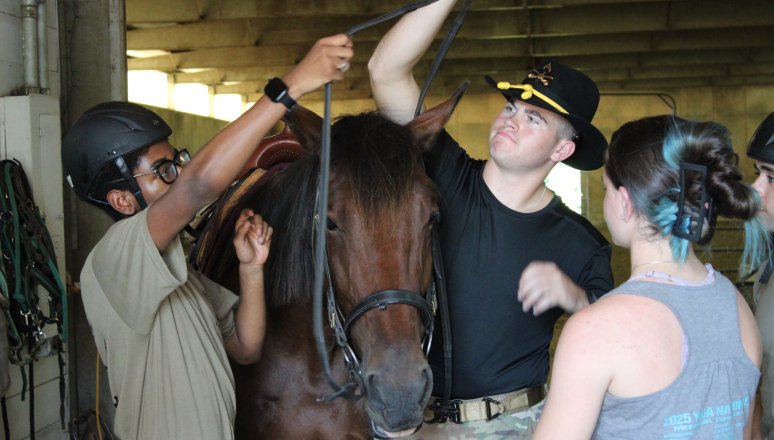 Cadets groom and prepare a horse inside a stable.