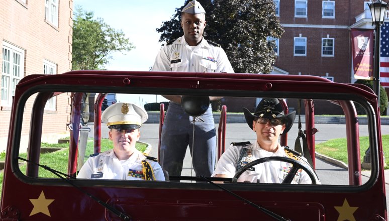 Cadet drives a vintage military vehicle with another cadet standing behind.