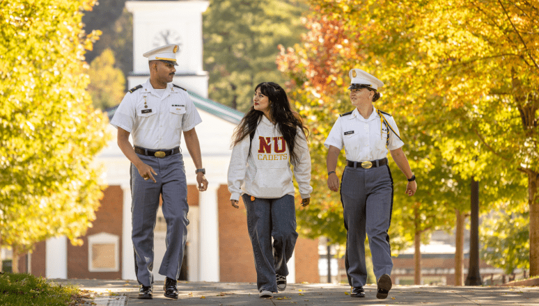 Three students walking together on campus surrounded by yellow fall foliage.