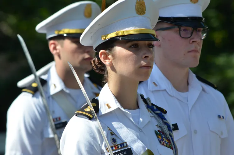 Female cadet in formation with sabers.