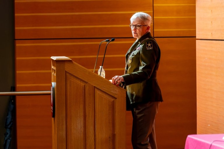 LTG Laura Potter stands behind a podium as she speaks to a crowd in an auditorium.