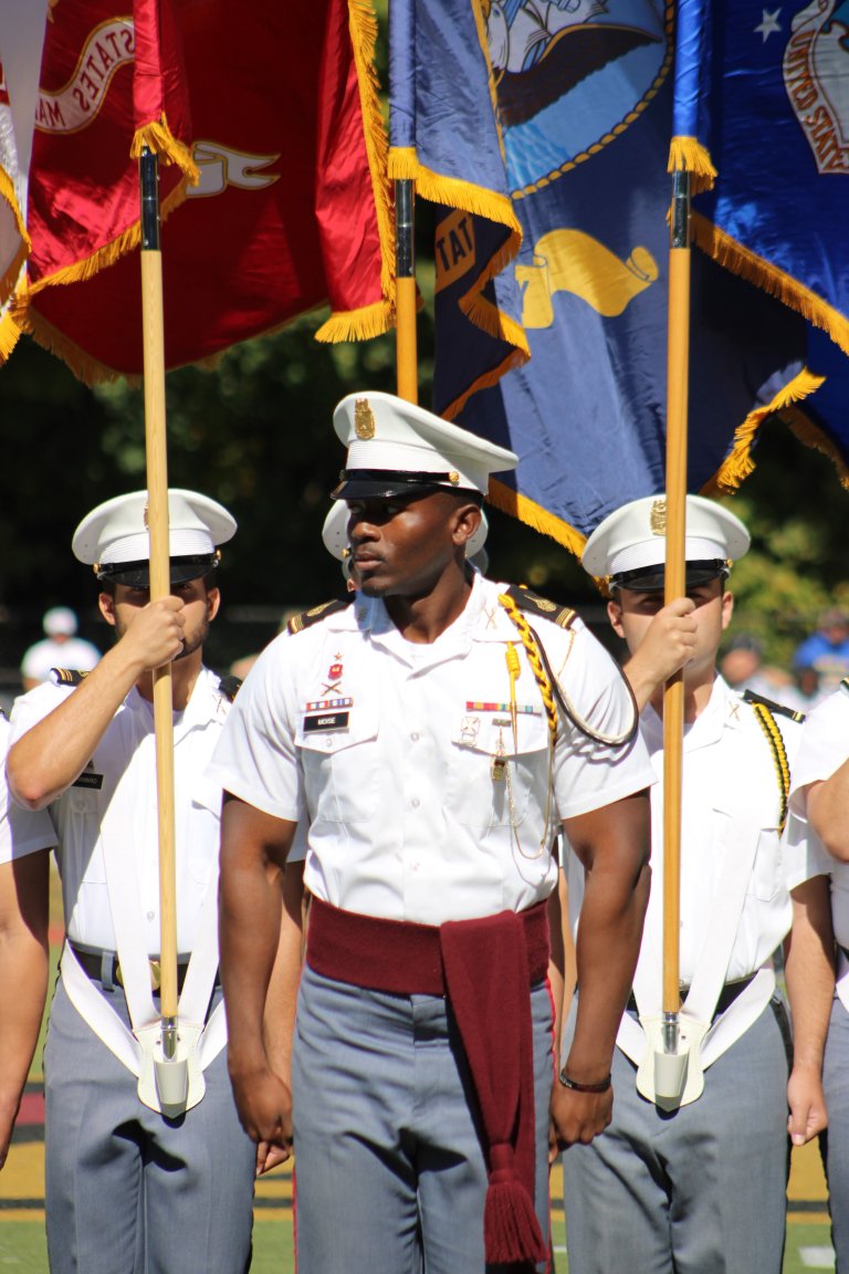 Cadet color guard stands at attention holding service flags during ceremony.