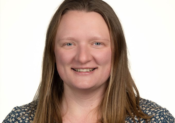 Person with medium colored straight shoulder length hair, light complexion, wearing a green patterned shirt.