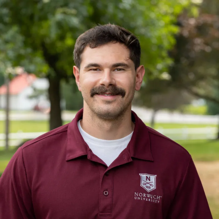 Portrait of Dennis Pollicino outside wearing a maroon Norwich polo.