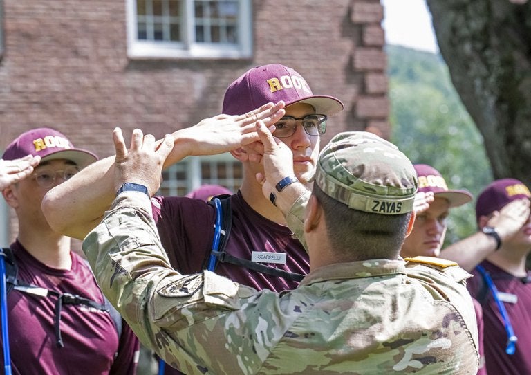 Rooks salute as a service member in uniform guides one Rook's hand position.