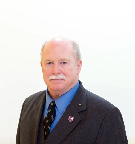 Person in a dark suit, blue shirt, and patterned tie poses against a plain light background.