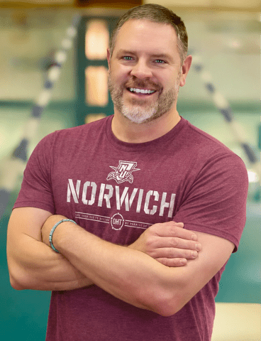 Portrait of a person wearing a Norwich T-shirt with arms crossed.