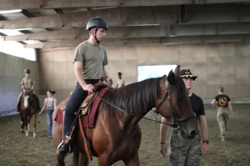 Cadets ride horses inside an arena.