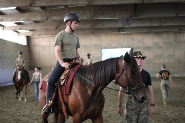 Cadets ride horses inside an arena.