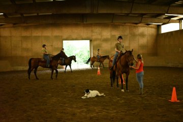 Group of cadets practice riding in indoor arena.