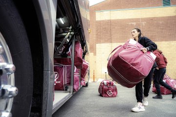 Norwich University women’s ice hockey players load large equipment bags onto team bus before traveling to NCAA Frozen Four