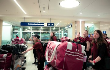 Norwich women’s hockey team pushes multiple luggage carts filled with equipment bags through airport terminal 