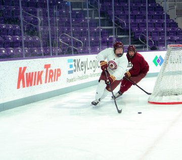 Two Norwich women’s hockey players skate hard along boards chasing puck during practice at Anderson Arena 