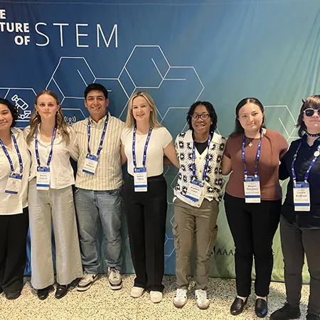 Seven conference attendees wearing name badges stand in front of a banner reading "The Future of STEM."